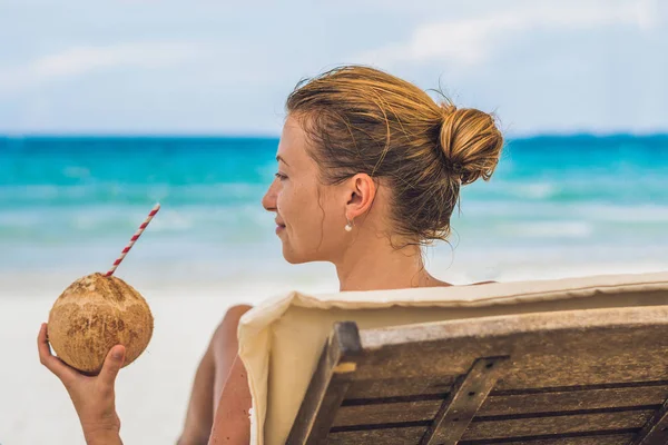 Mujer joven bebiendo leche de coco en Chaise-longue en la playa . —  Fotos de Stock