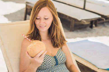 Genç kadın plajda şezlong üzerinde Hindistan cevizi sütü içme.
