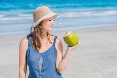 Genç kadın kumsalda Hindistan cevizi sütü içme.