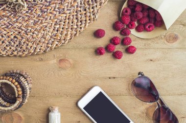 Yaz tatili, tatil, gevşeme kavramı. Ahududu, hasır şapka, cep telefonu, akıllı telefon, yukarıdan güneş gözlüğü, üstten görünüm, ahşap arka plan üzerinde düz yatıyordu. Serbest metin kopya alanı ile renkli arka plan. Yaz vibes kavramı.