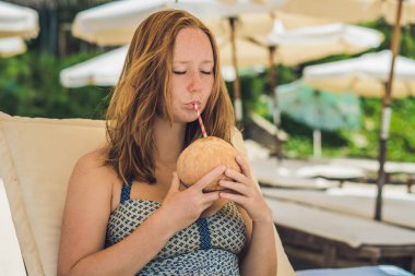 Genç kadın plajda şezlong üzerinde Hindistan cevizi sütü içme.