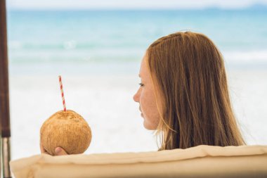 Genç kadın plajda şezlong üzerinde Hindistan cevizi sütü içme.