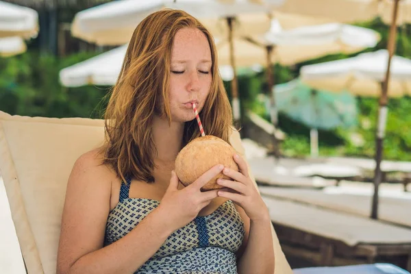 Genç kadın plajda şezlong üzerinde Hindistan cevizi sütü içme.