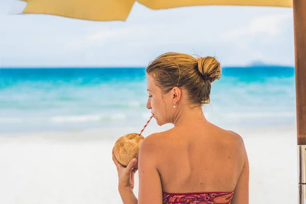 Jovem mulher bebendo leite de coco em Chaise-longue na praia . — Fotografia de Stock