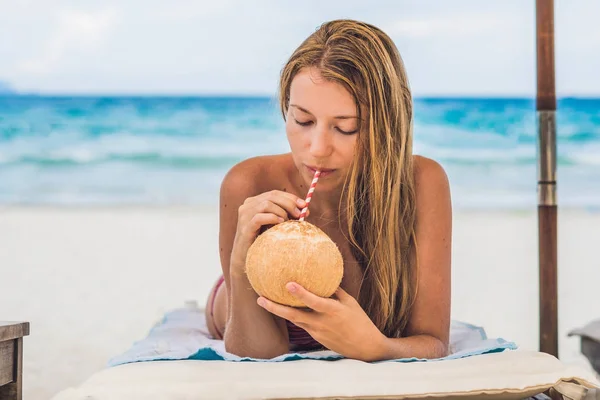 Jovem mulher bebendo leite de coco em Chaise-longue na praia . — Fotografia de Stock