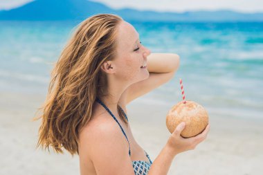 Genç kadın kumsalda Hindistan cevizi sütü içme.