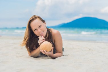 Genç kadın kumsalda Hindistan cevizi sütü içme.