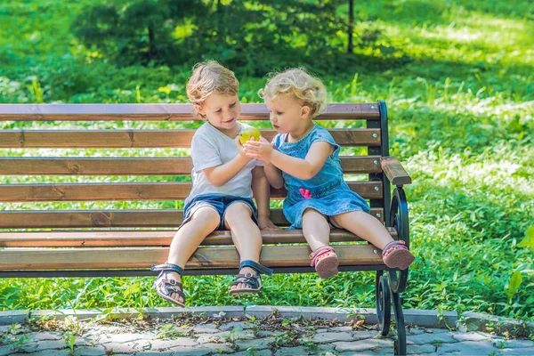 Yeni yürümeye başlayan çocuklar çocuk ve deniz kenarında bir bankta oturan kız ve bir elma yemek.