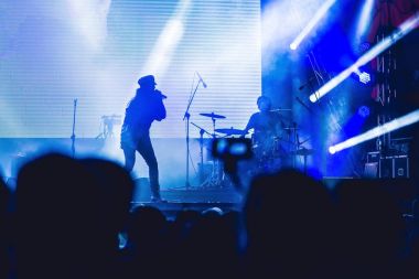 Konser aydınlık bir sahne karşı büyük bir kalabalığa silüeti. Gece zaman rock konseri insanlarla eğlenmek eller havada yukarı kaldırarak ve müzisyenler tezahürat