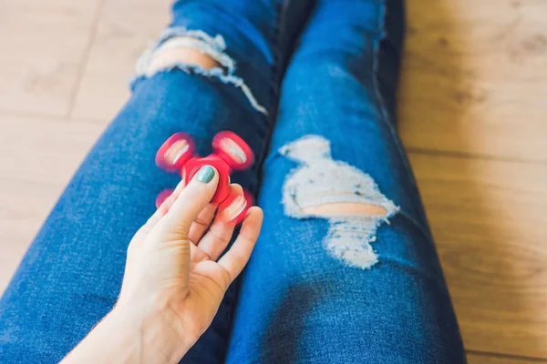 Girl teenager in holey jeans holds in hands and plays with spinner — Stock Photo, Image