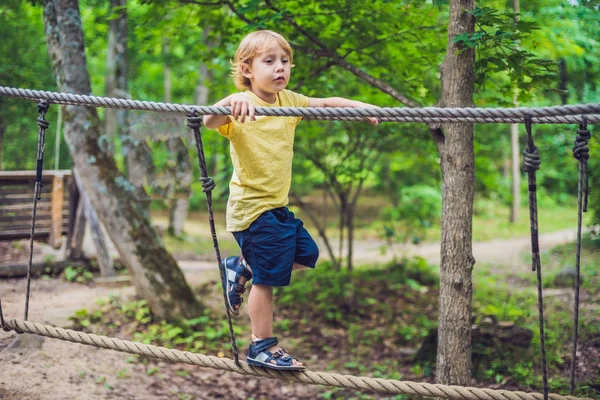 Retrato de menino bonito caminha em uma ponte de corda em um parque de corda de aventura — Fotografia de Stock