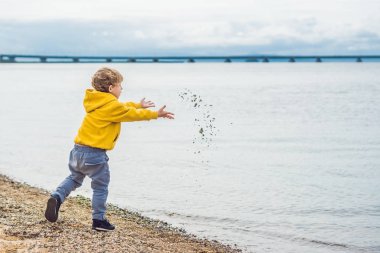Young boy throwing stones in sea water clipart