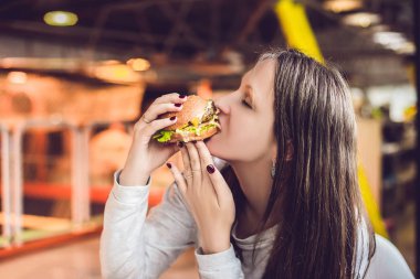 Genç kadın yeme hamburger kadın yeme abur cubur, yağlı yiyecek hamburger.