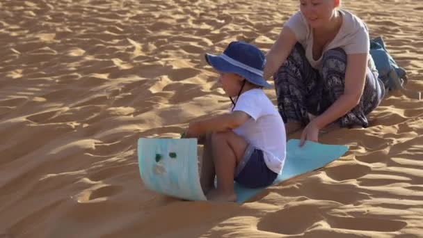 小男孩骑着雪橇沿着红色沙漠的沙丘 — 图库视频影像