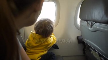 Bir çocuk bir penceresine bakarak bir uçağın gemide sarı ceketli kadeh Slowmotion