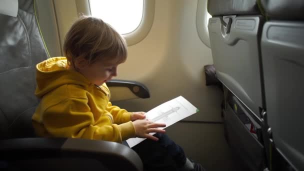 Мальчик с наушниками, смотрящий и слушающий в летных развлечениях на борту самолета — стоковое видео