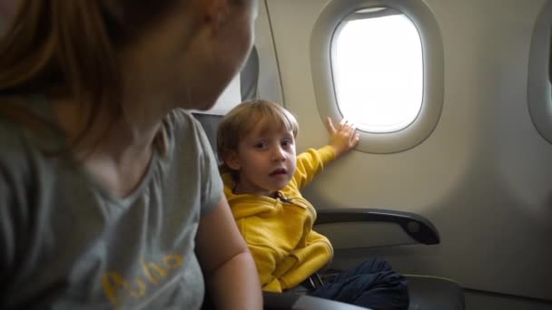 Fotografía en cámara lenta de un niño con chaqueta amarilla a bordo de un avión mirando a una ventana — Vídeos de Stock