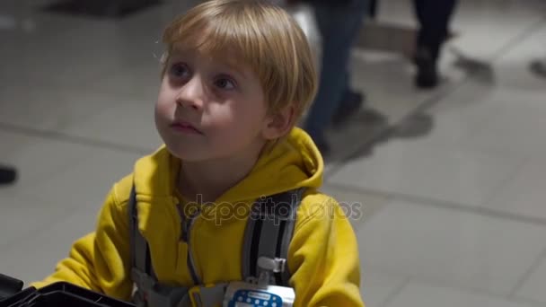台車の上に立って彼女の息子と一緒に空港で歩いている若い女性のステディカム ショット — ストック動画