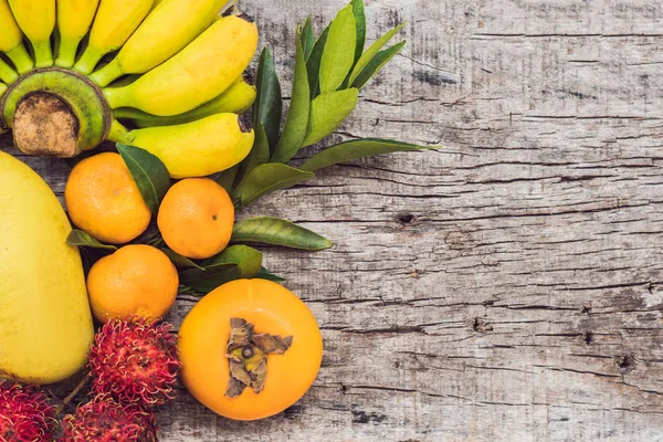 Kleurrijke vruchten op witte houten tafel, bananen, carambola's, mango, papaya, Mandarijn, ramboetan, pamela, ruimte voor tekst kopiëren — Stockfoto