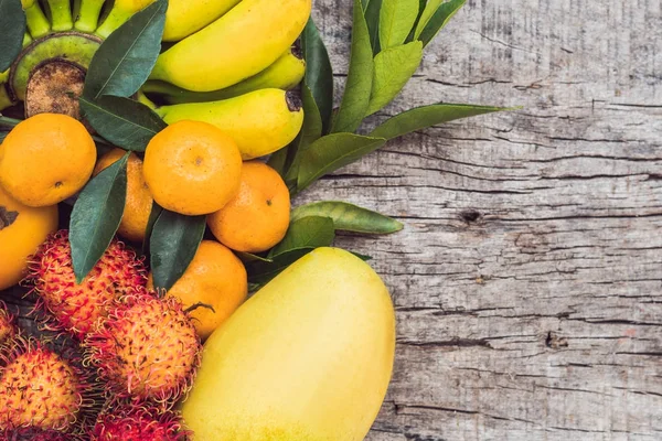 Kleurrijke vruchten op witte houten tafel, bananen, carambola's, mango, papaya, Mandarijn, ramboetan, pamela, ruimte voor tekst kopiëren — Stockfoto
