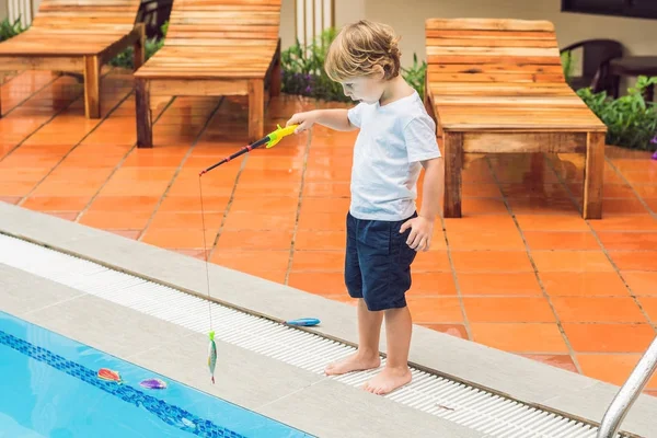 Een schattig jongetje is het vangen van een vis speelgoed in het zwembad — Stockfoto