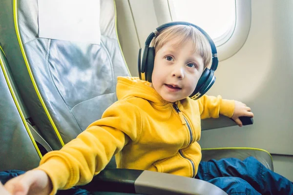 Fiú fejhallgató, nézni és hallgatni a repülés szórakoztató repülőgép fedélzetén — Stock Fotó