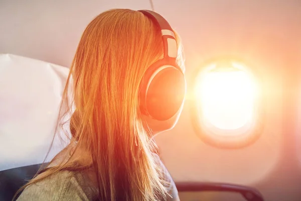 Passagier im Flugzeug über Kopfhörer. Frau in Flugzeugkabine hört Musik über Kopfhörer. — Stockfoto