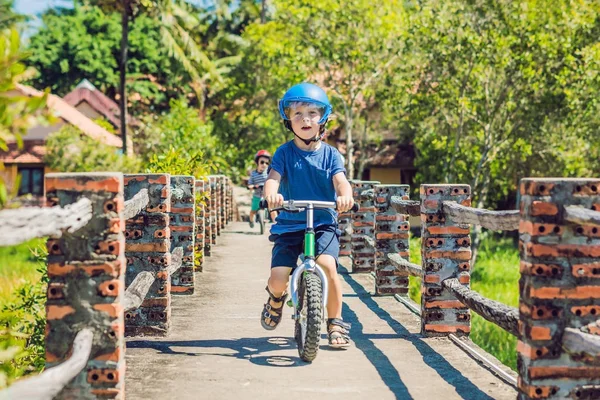 İki küçük çocuklar çocuklar eğleniyor denge bisiklet üzerinde bir ülke tropikal yolda.