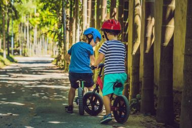 İki küçük çocuklar çocuklar eğleniyor denge bisiklet üzerinde bir ülke tropikal yolda.
