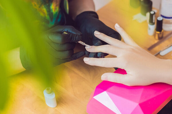 Closeup finger nail care by manicure specialist in beauty salon. Manicurist paints nails with nail polish.