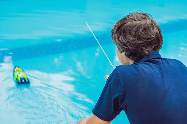 Man playing with a remote controlled boat in the pool.