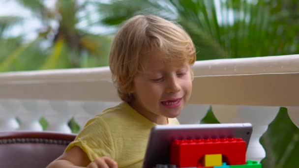 Мальчик в тропиках разговаривает с друзьями и семьей по видеосвязи с помощью планшета и беспроводных наушников — стоковое видео