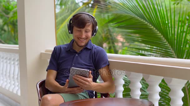 Homme dans les tropiques parler avec des amis et de la famille sur appel vidéo à l'aide d'une tablette et écouteurs sans fil — Video