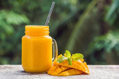 Mango smoothie cam Mason kavanoza ve mango yeşil bir backgro üzerinde