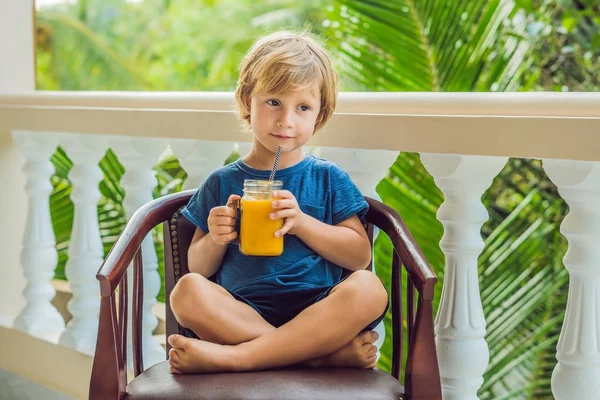 Мальчик пьет сочный смузи из манго в стеклянной банке из каменщика с S — стоковое фото