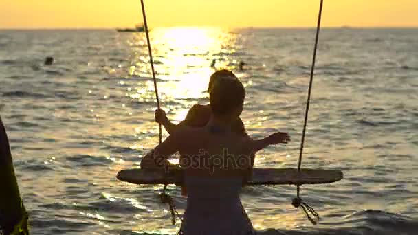 Щаслива жінка кладе сина на мотузку з райським тропічним морем на задньому плані — стокове відео