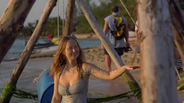 Молодая женщина размахивает своим счастливым сыном на деревянных качелях в море на закате — стоковое видео