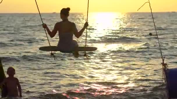 Mujer feliz balanceándose y relajándose en un columpio de cuerda con un paraíso tropical en el fondo — Vídeos de Stock