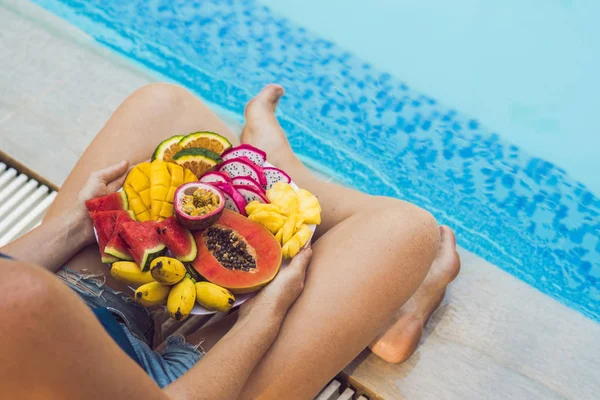 Молода жінка розслабляється і їсть фруктову тарілку біля басейну готелю. Електронна — стокове фото