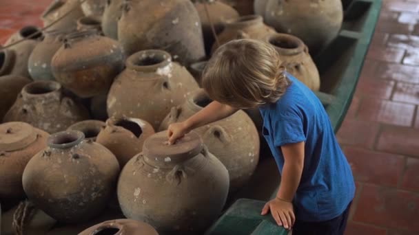 Little boy visits exposition in national museum on Phu Quoc island Vietnam, he looks at an ancient boat filled with ceramic jugs — Stock Video