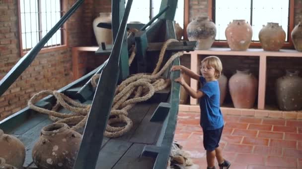 Menino visita exposição no museu nacional em Phu Quoc ilha Vietnã, ele olha para um barco antigo cheio de jarros de cerâmica — Vídeo de Stock