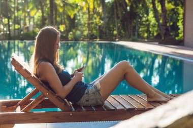 Mutlu smartphone kadın Yüzme Havuzu rahatlatıcı. Yaz lüks tatilde dinlenirken şarkıları çalmak için onun hareket eden telefon app 4 g veri kullanan güzel kız.