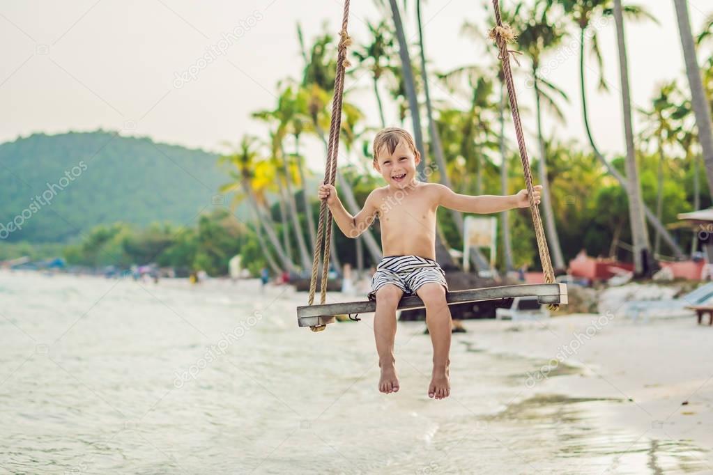 Happy boy sit on swing at the sea shore on sunset.