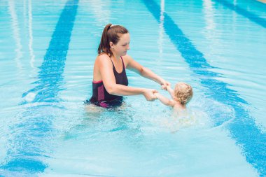 Genç anne küçük oğlu, öğretmek bir yüzme havuzunda yüzmeyi.