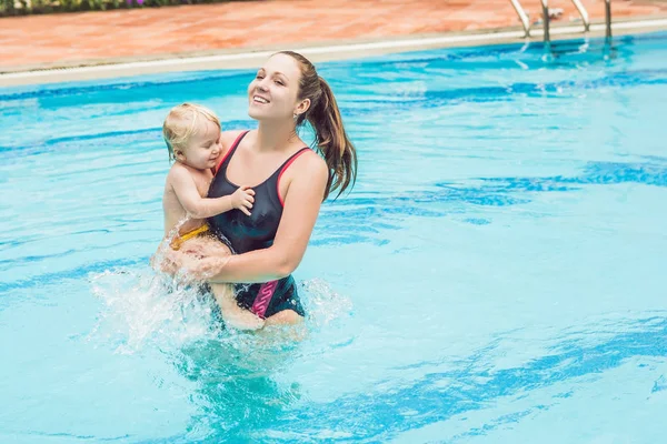 Young mother teach her little son, how to swim in a swimming pool.