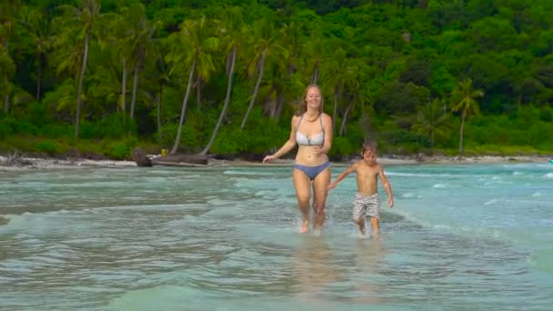 Молодая любящая мать и ее маленький сын играют на пляже — стоковое видео