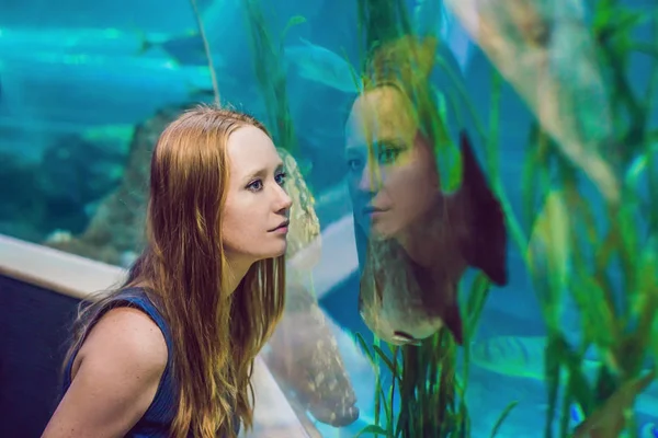 Young woman looking at fish in a tunnel aquarium