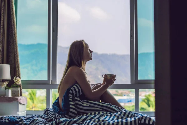 young happy woman woke up in the morning in the bedroom by the window with beautiful mountain views.