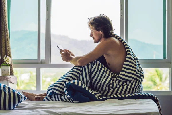 Man woke up in the morning and reads the news on the tablet in the background of a window with a view to the mountains.