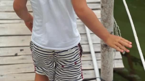 Уповільнення стійкої камери знімок хлопчика, що йде по дерев'яній прогулянці над морем до ресторану — стокове відео